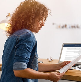 Woman at computer with document in hand
